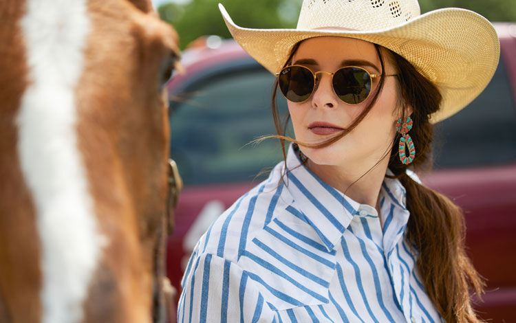 A woman staring wearing sunglasses leading a horse.